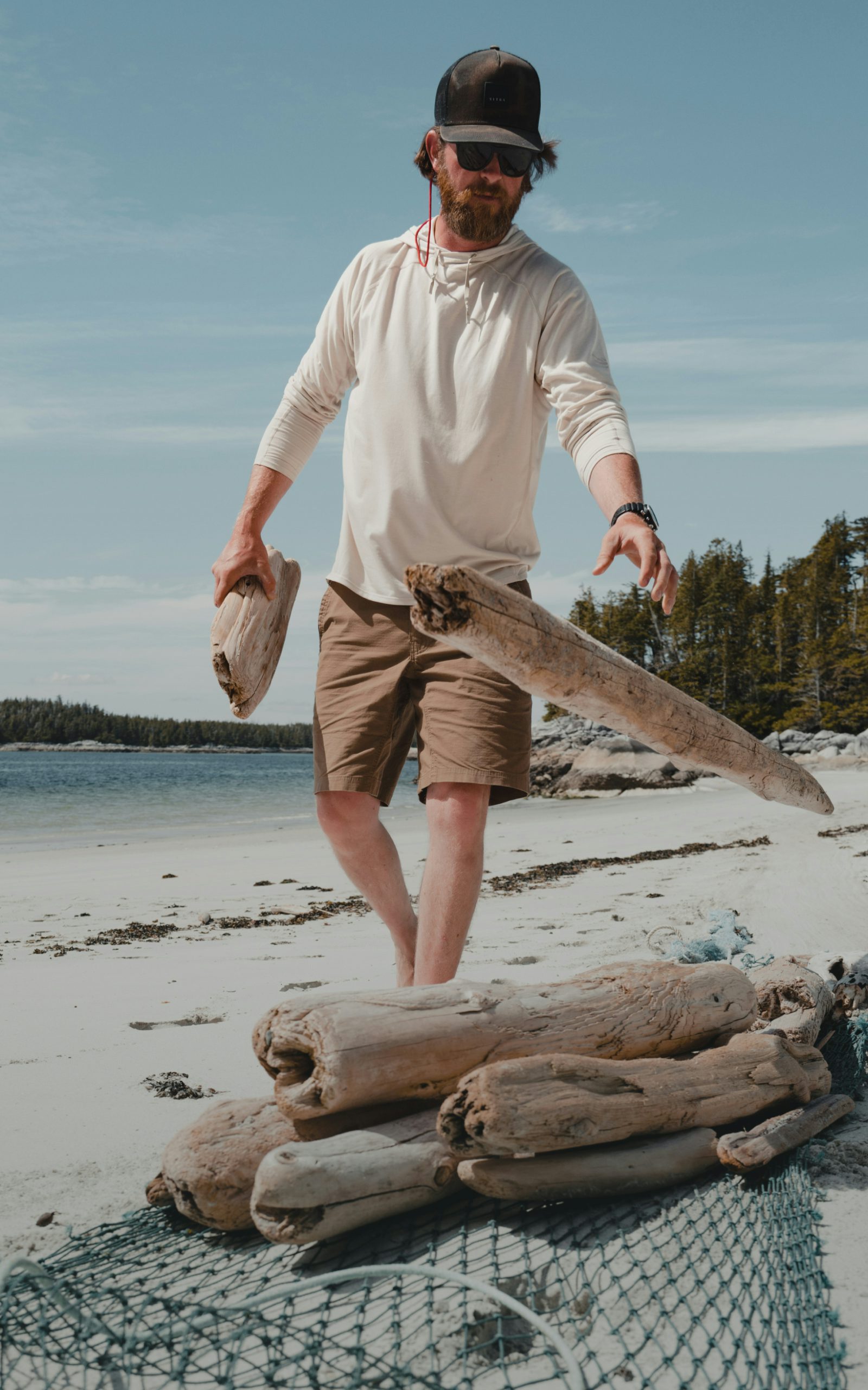 Connor Gabbott gathering driftwood on the beach for a fire in the Radiant Hoodie in Opal | SITKA Gear