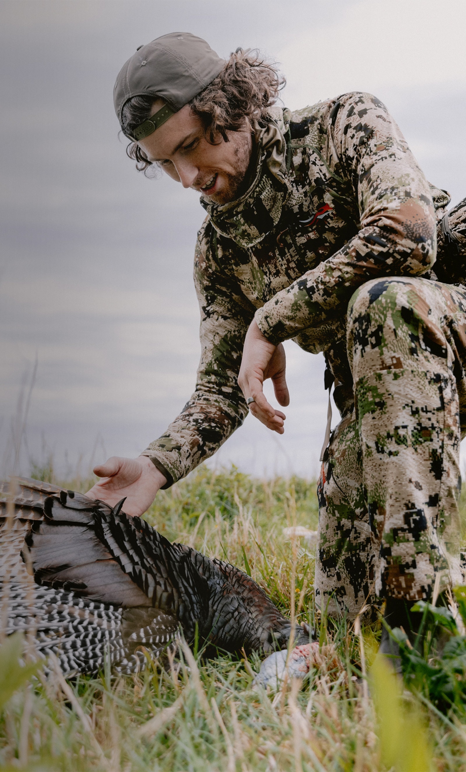 Beau Brooks kneeling over his harvested turkey in the Equinox Guard System in Optifade subalpine | SITKA Gear