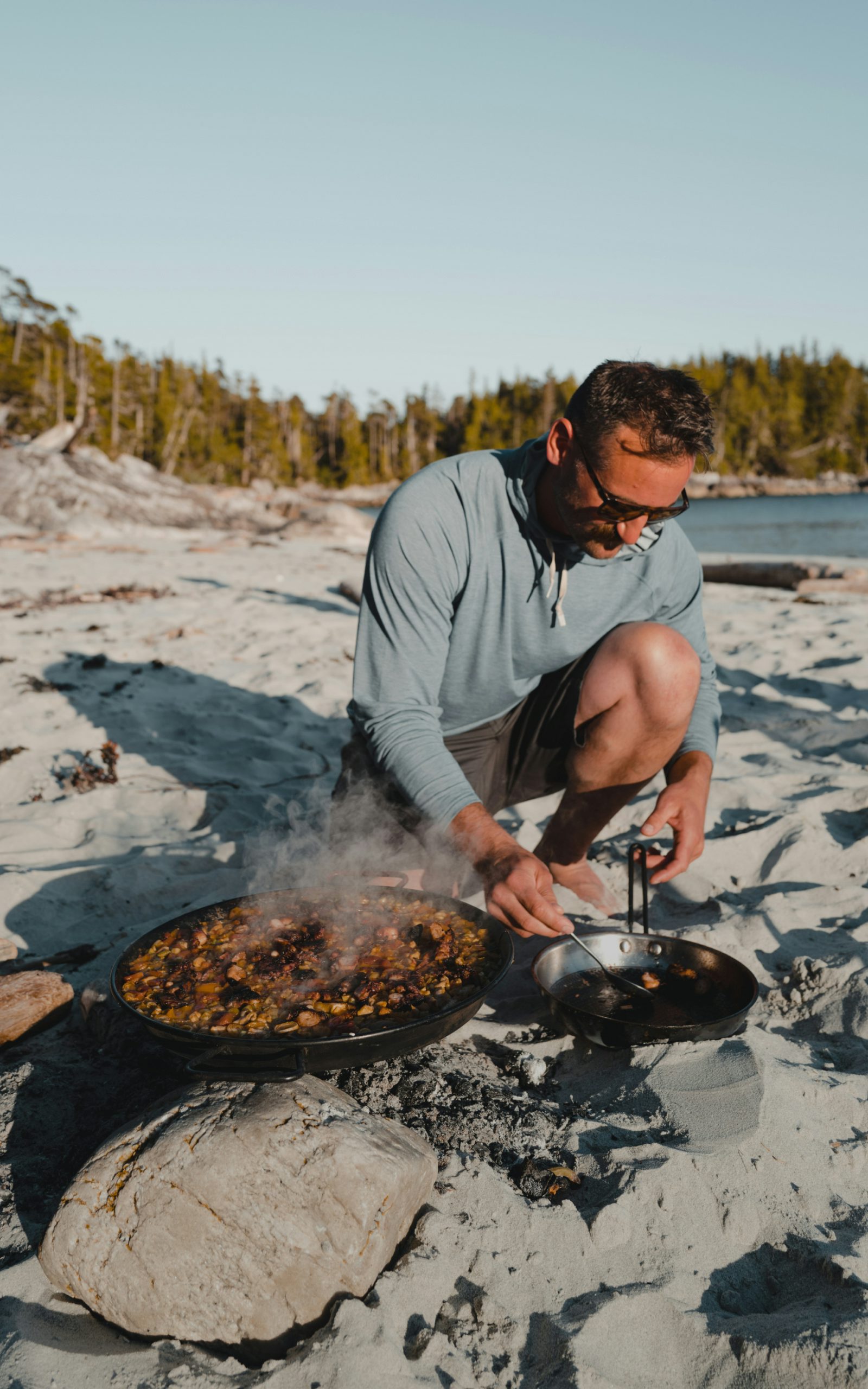 Man cooking on the beach wearing the Radiant Hoody in Blue Haze | SITKA Gear