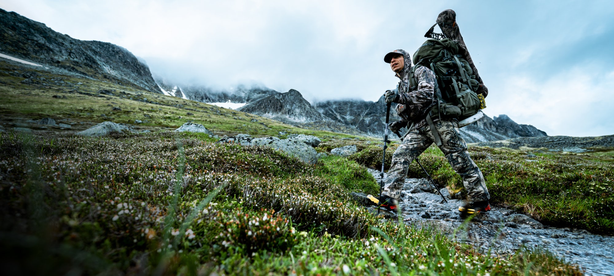 Adam Foss crossing a river in the Dewpoint Collection in Optifade Open Country | SITKA Gear