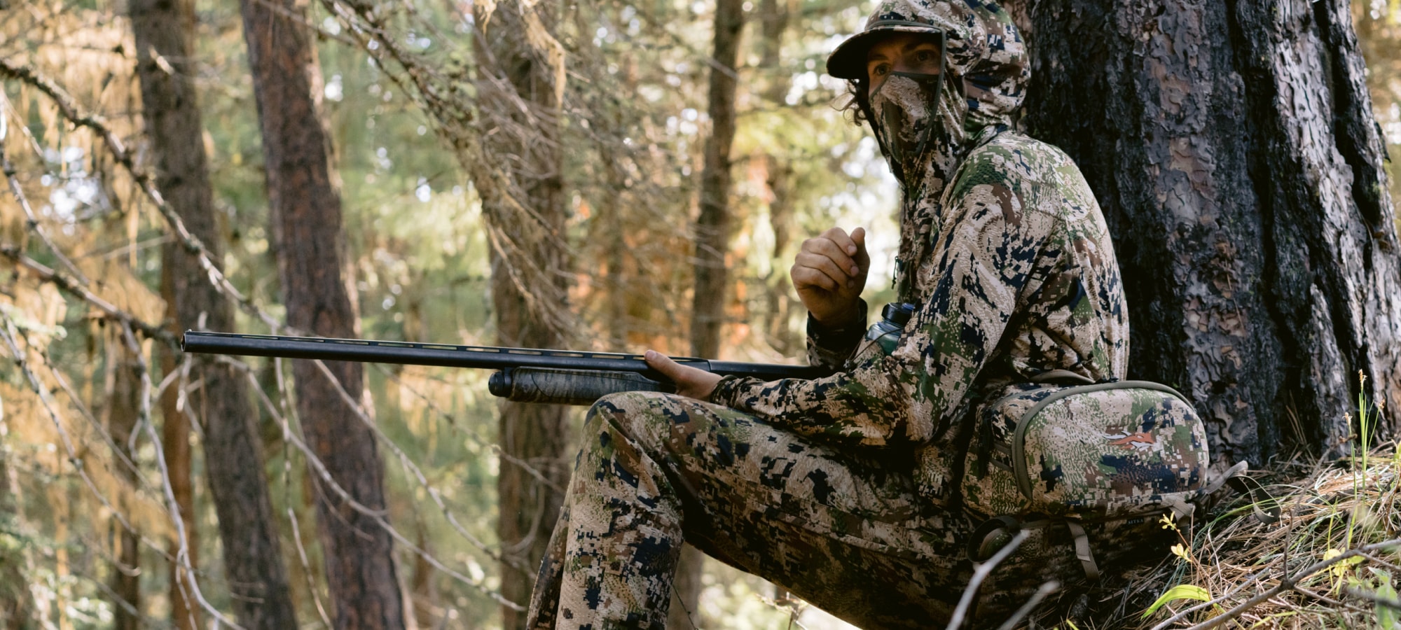 Beau Brooks sitting at the base of a tree wearing the Turkey Tool Belt and Equinox Guard System in Optifade Subalpine | SITKA Gear