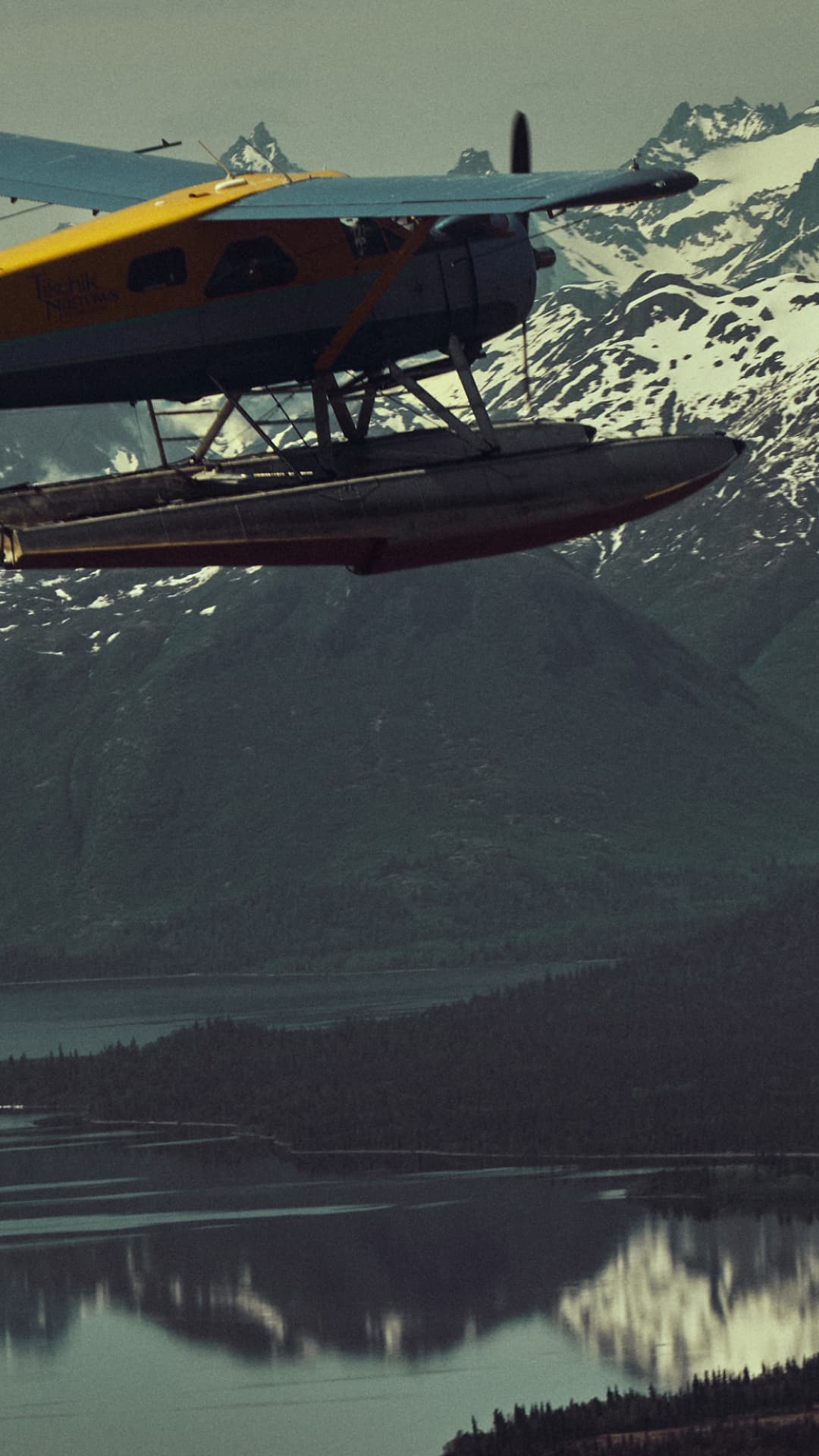 A sea plane flys high above the water through a hazy mountain range somewhere in a remote location.