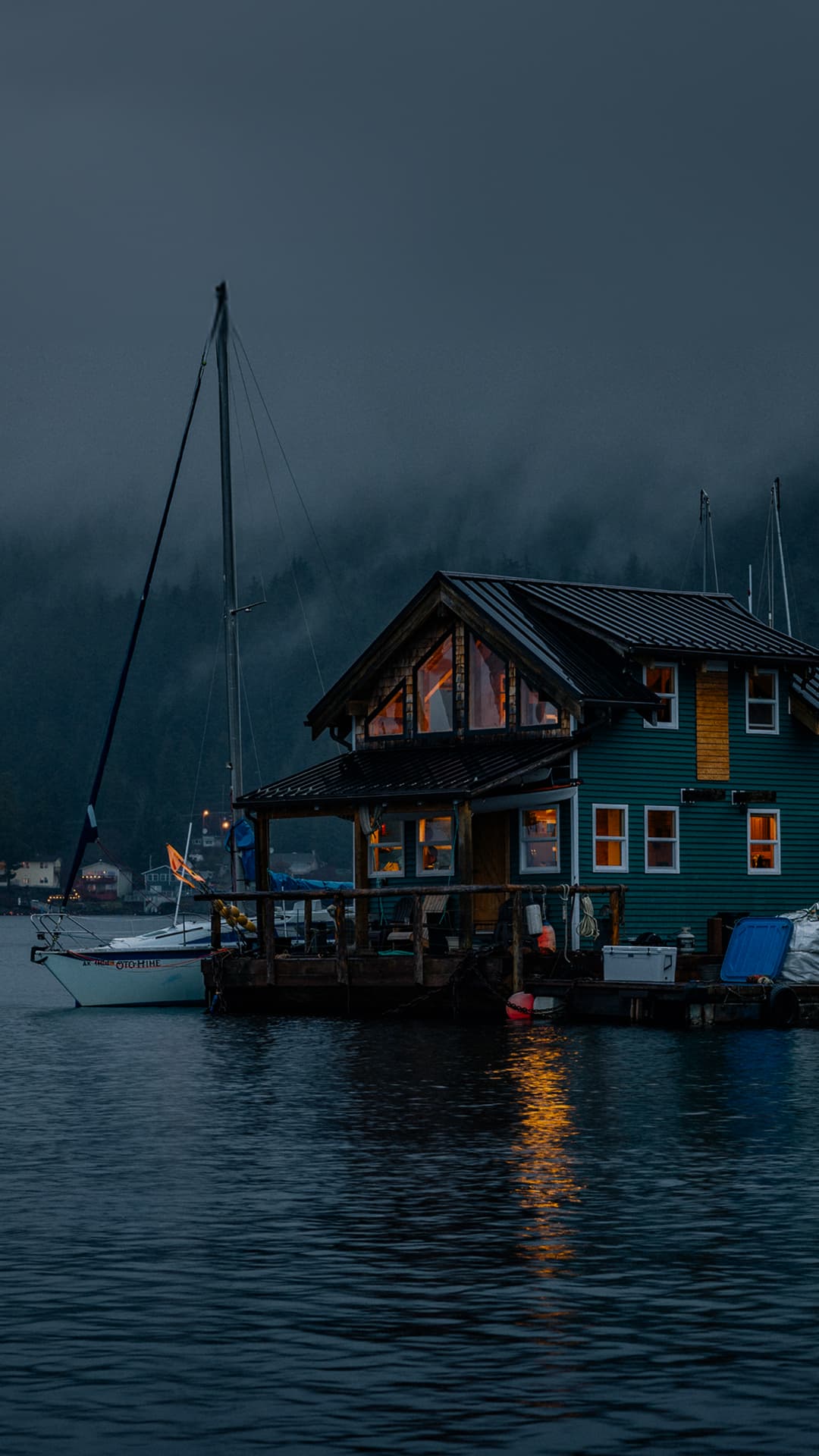 A house built on a dock on top the water with misty mountains behind it.