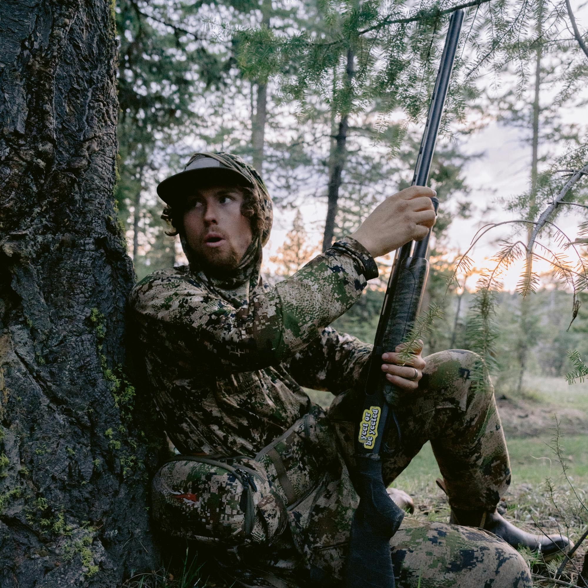Beau Brooks sitting against a tree calling to turkeys in the Equinox Guard System in Optifade Subalpine | SITKA Gear