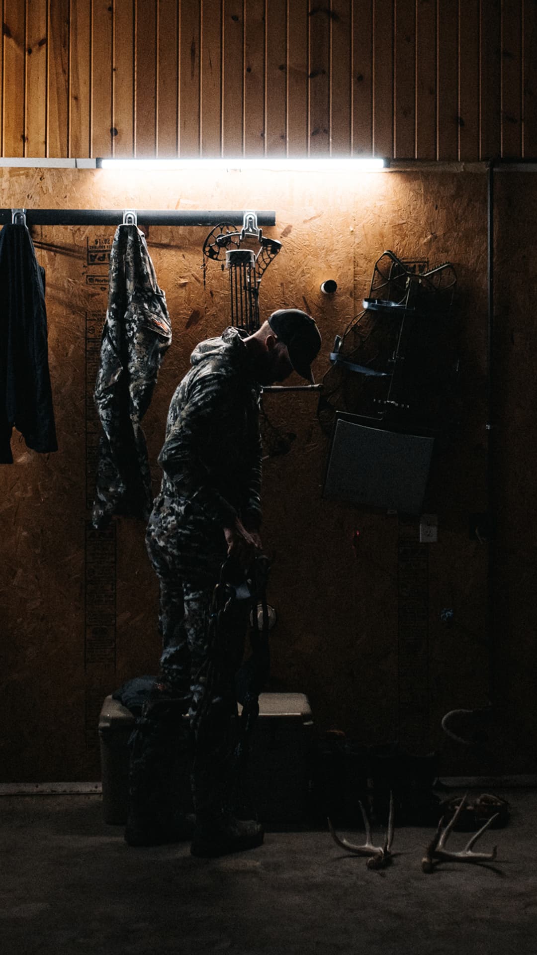 A man getting his gear ready in a gear garage with other gear hanging on hooks.