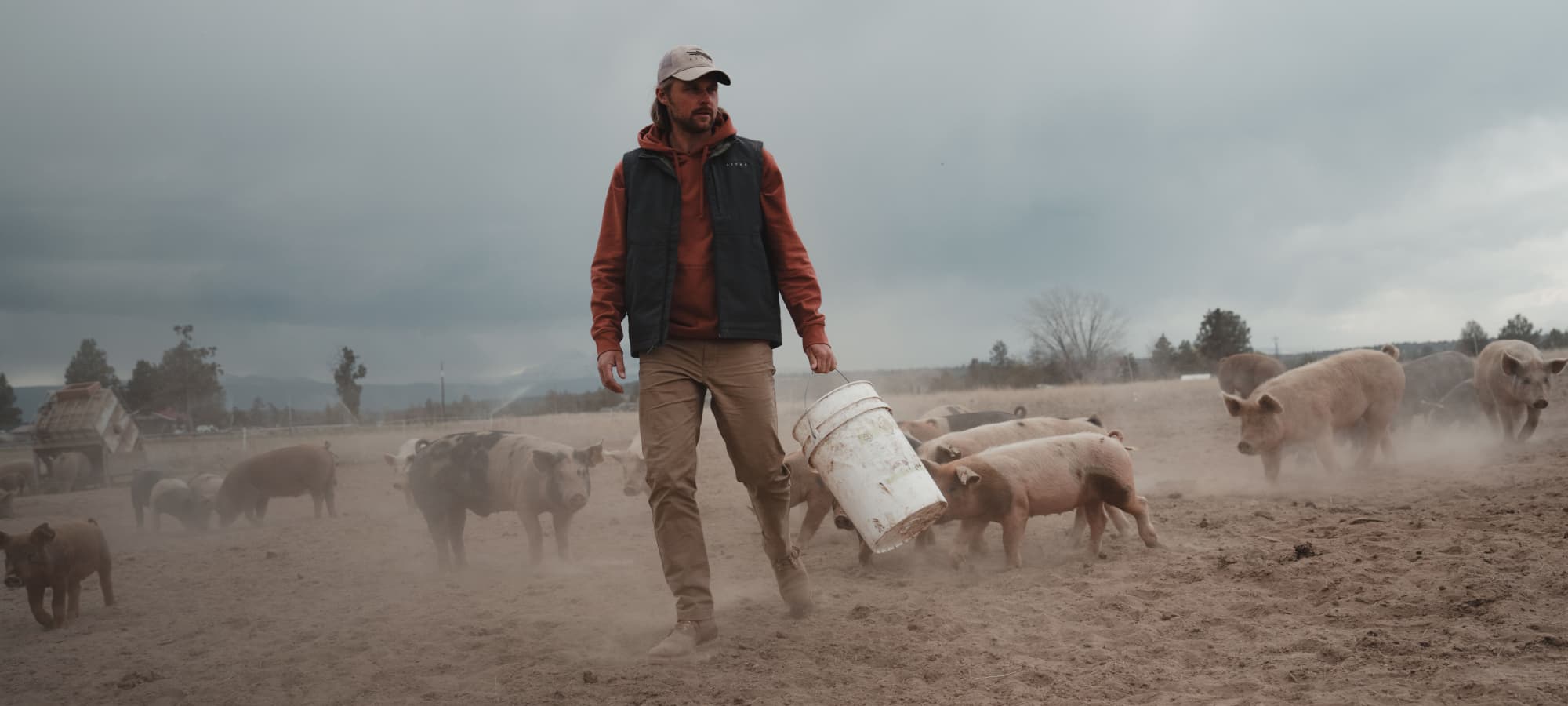 Man feeding pigs in the Grindstone Vest in Obsidian from the Workwear Collection | SITKA Gear