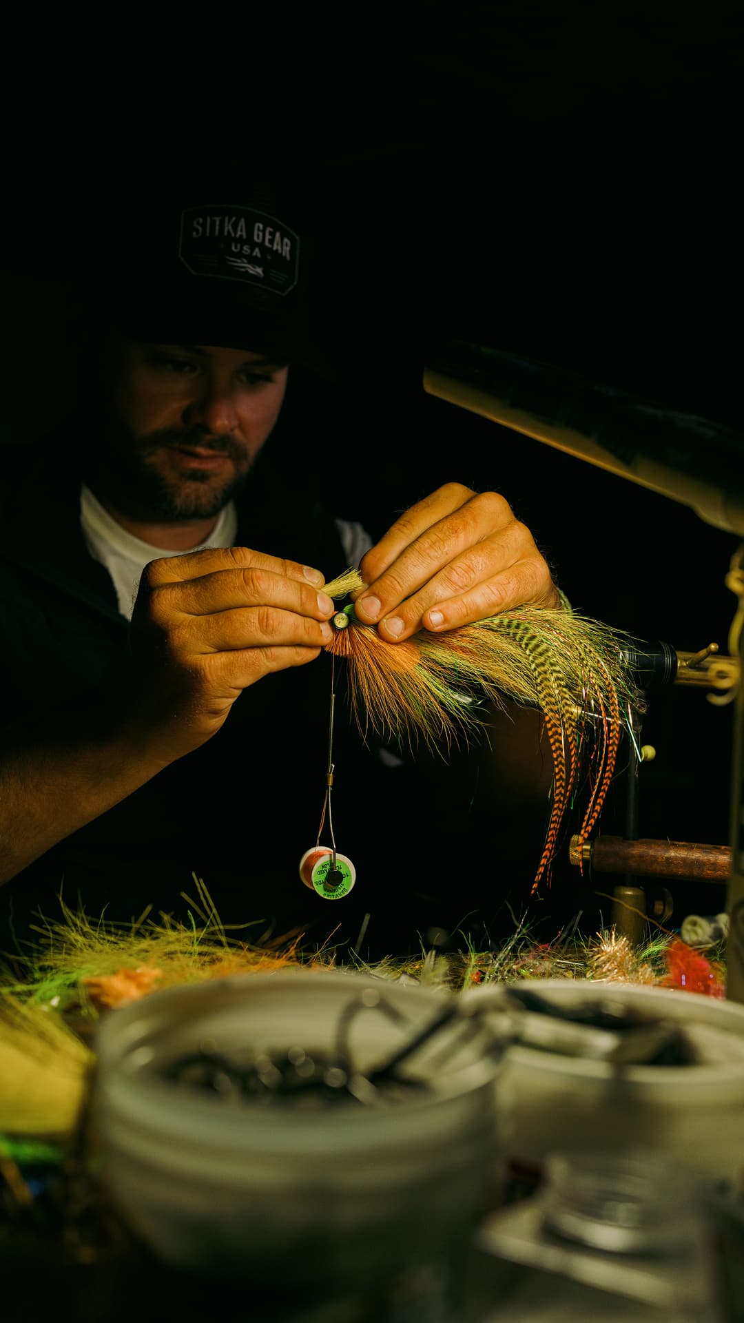 A man inspecting his fishing fly under dim warm light.