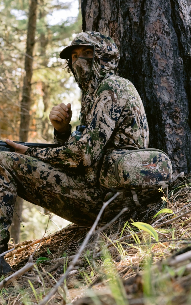 Beau Brooks sitting at the base of a tree wearing the Turkey Tool Belt and Equinox Guard System in Optifade Subalpine | SITKA Gear