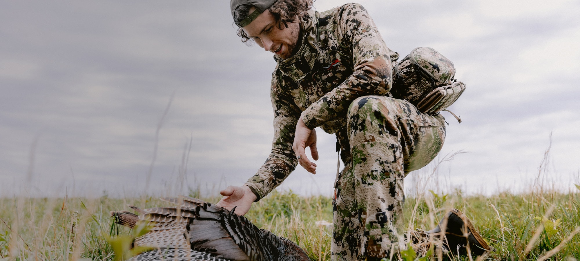 Beau Brooks kneeling over his harvested turkey in the Equinox Guard System in Optifade subalpine | SITKA Gear